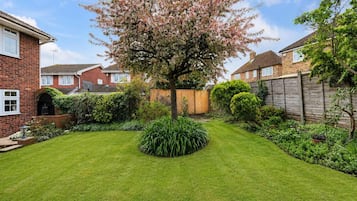 A residential garden with a well-maintained lawn, a variety of shrubs, and a flowering tree.