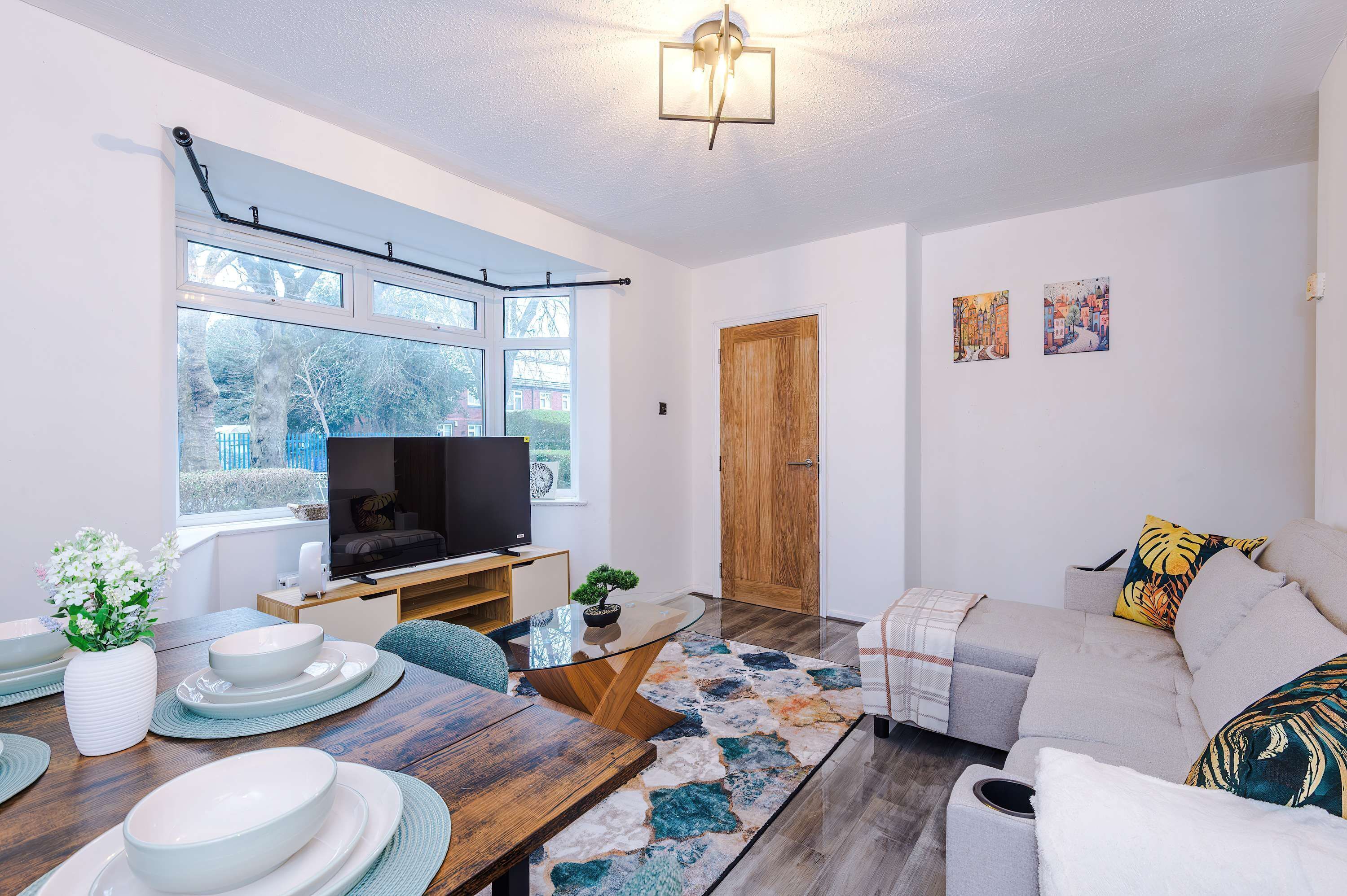 A modern living room with a flat-screen TV, a dining table with plates, a sofa, and a wooden door.