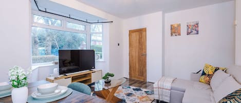 A modern living room with a flat-screen TV, a dining table with plates, a sofa, and a wooden door.