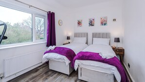 A hotel room with two beds, a window with curtains, a radiator, a clock, and artwork on the wall. - Large 3BR Near Airport Hospital Free Parking (Manchester)