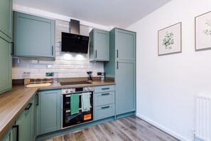 Een moderne keuken met lichtblauwe kastjes, een zwarte afzuigkap, een houten aanrechtblad en een inbouwoven.