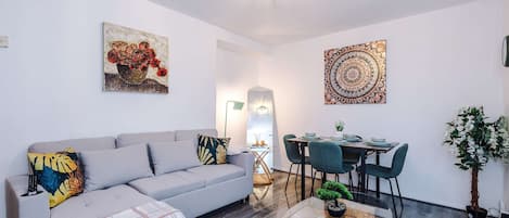 A living room with a grey sofa, a glass coffee table, and a dining area with a table and chairs.