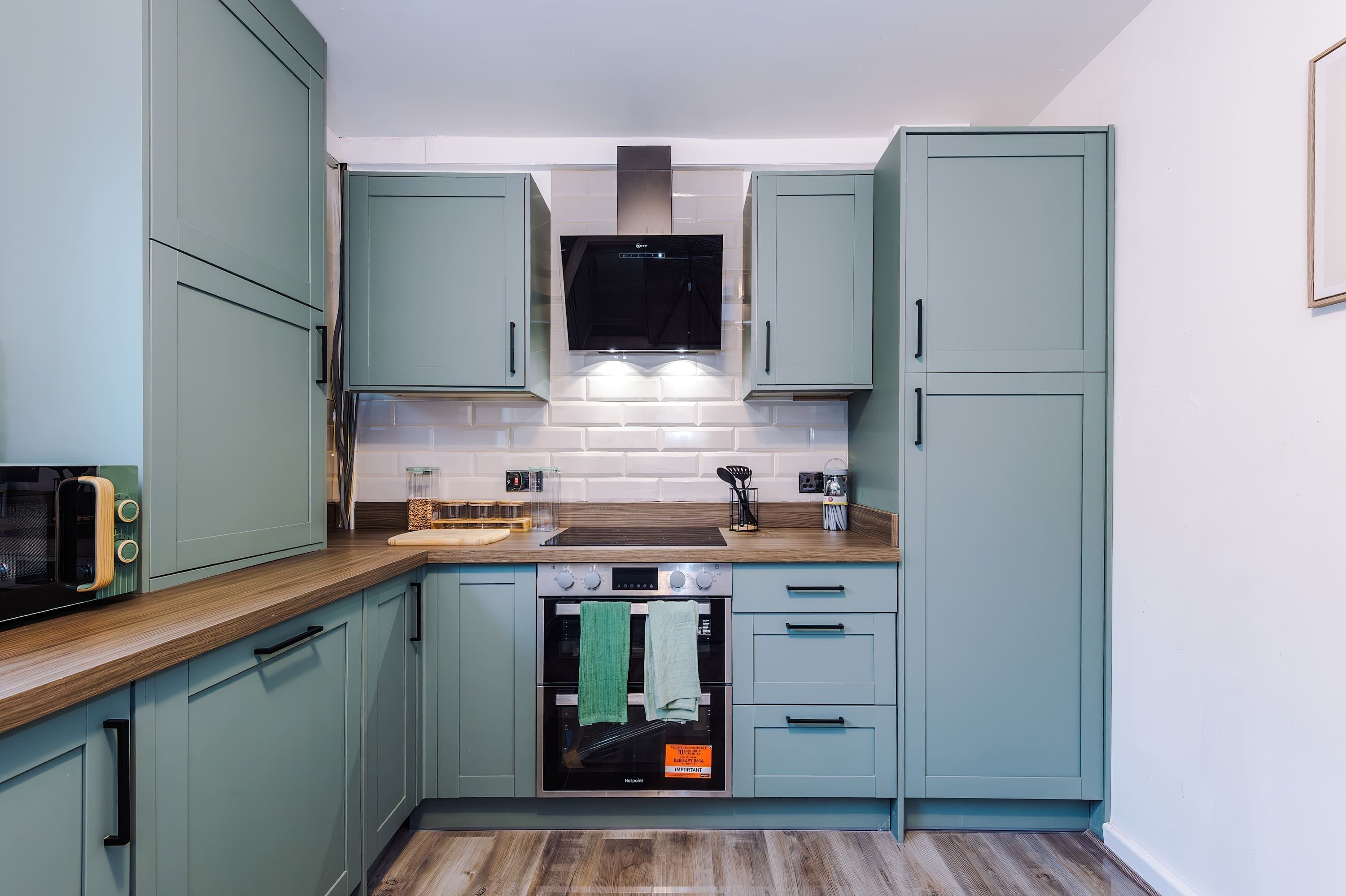 A compact kitchen with teal cabinets, a microwave, a stove, and a sink.