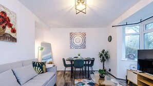 A modern living room with a grey sofa, a dining table with chairs, a wall-mounted artwork, a floor lamp, and a large window. - Large 3BR Near Airport Hospital Free Parking (Manchester)