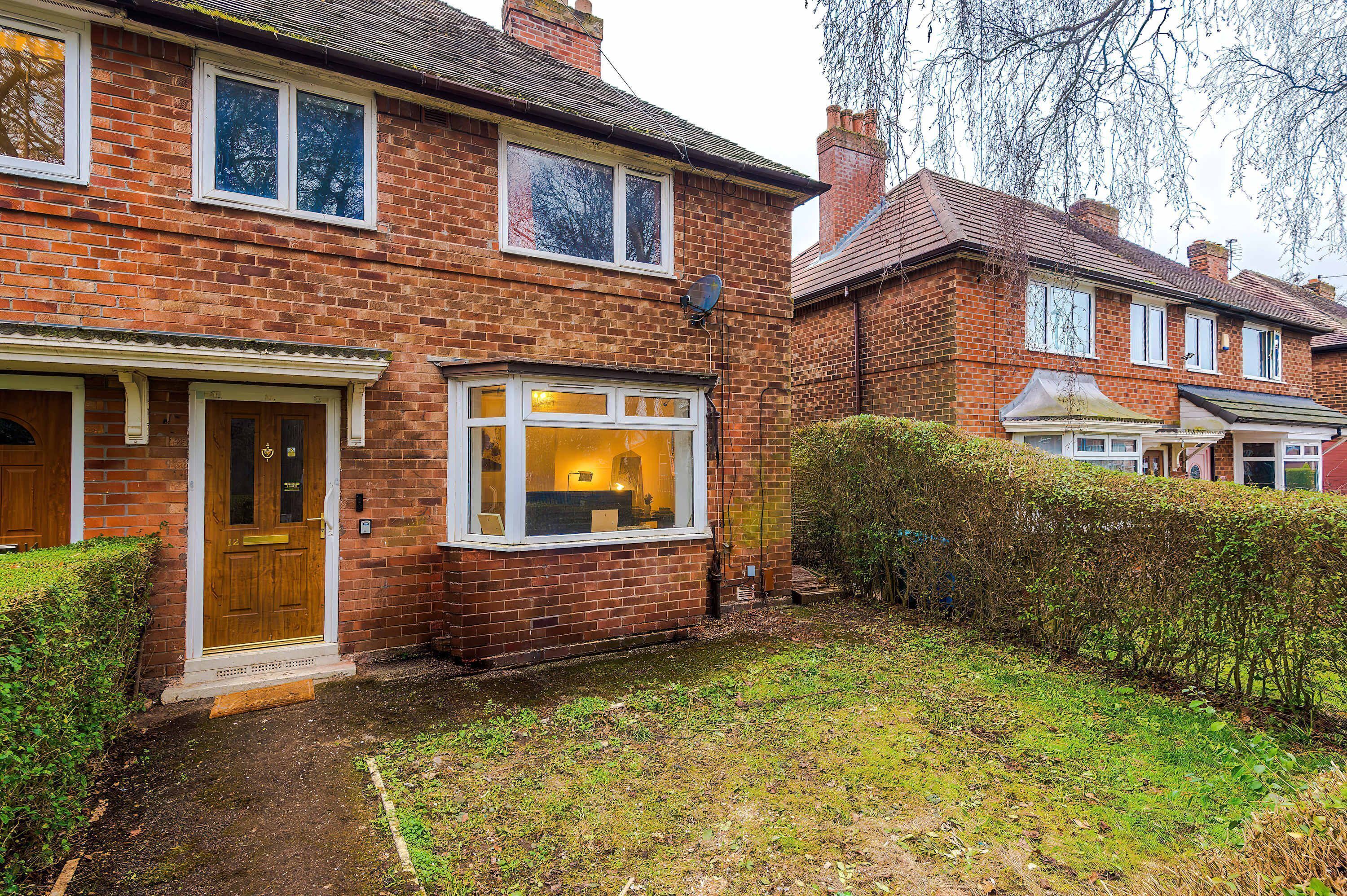 A brick house with a front door, a window with a view of the interior, and a small garden area.