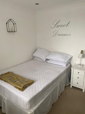 A neatly made bed with a quilted white mattress, a decorative throw blanket, and a bedside table with a lamp. - Large 6 Bed Windsor Stay Near Legoland M4 (Maidenhead)