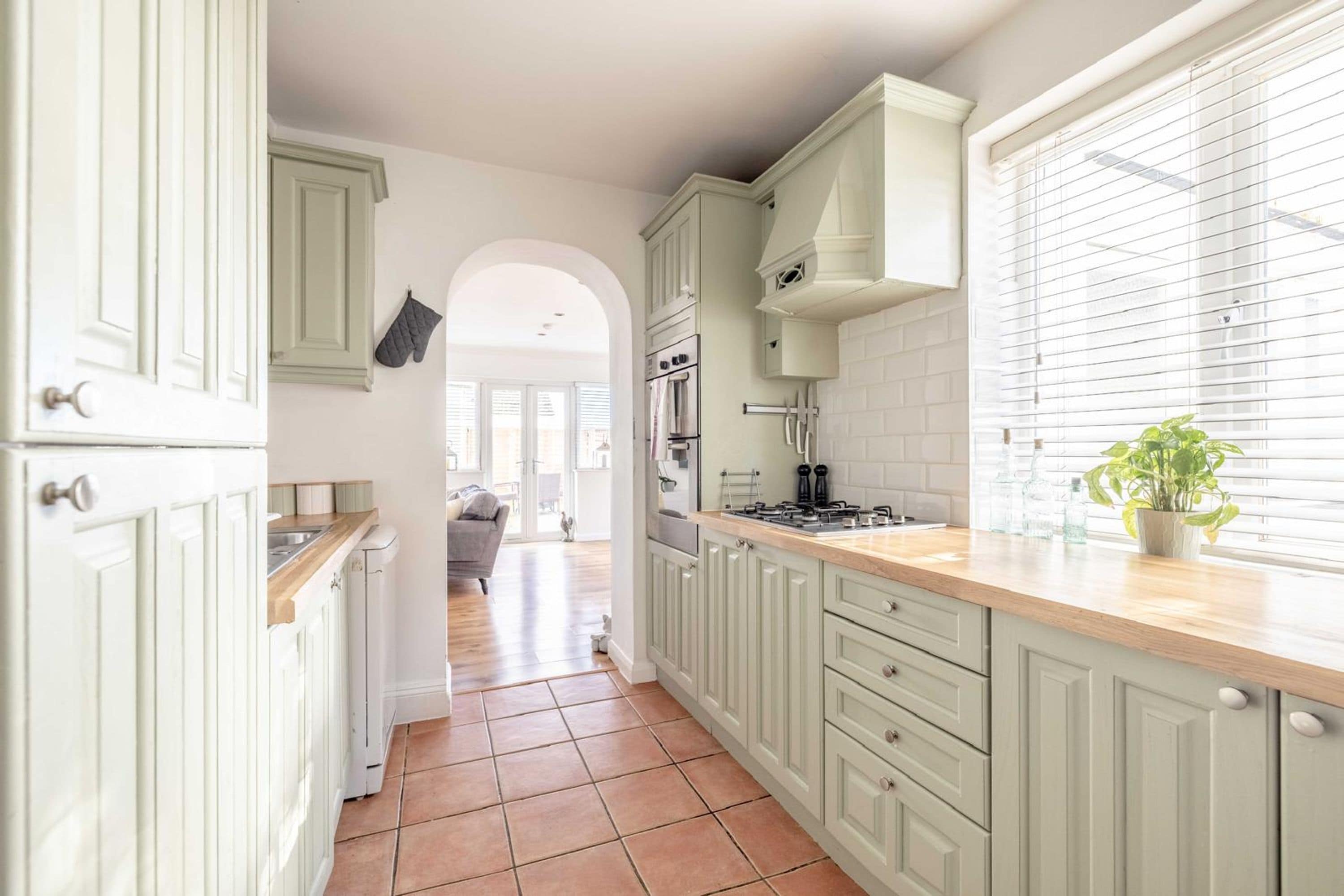A kitchen with white cabinets, a wooden countertop, and a window with blinds.