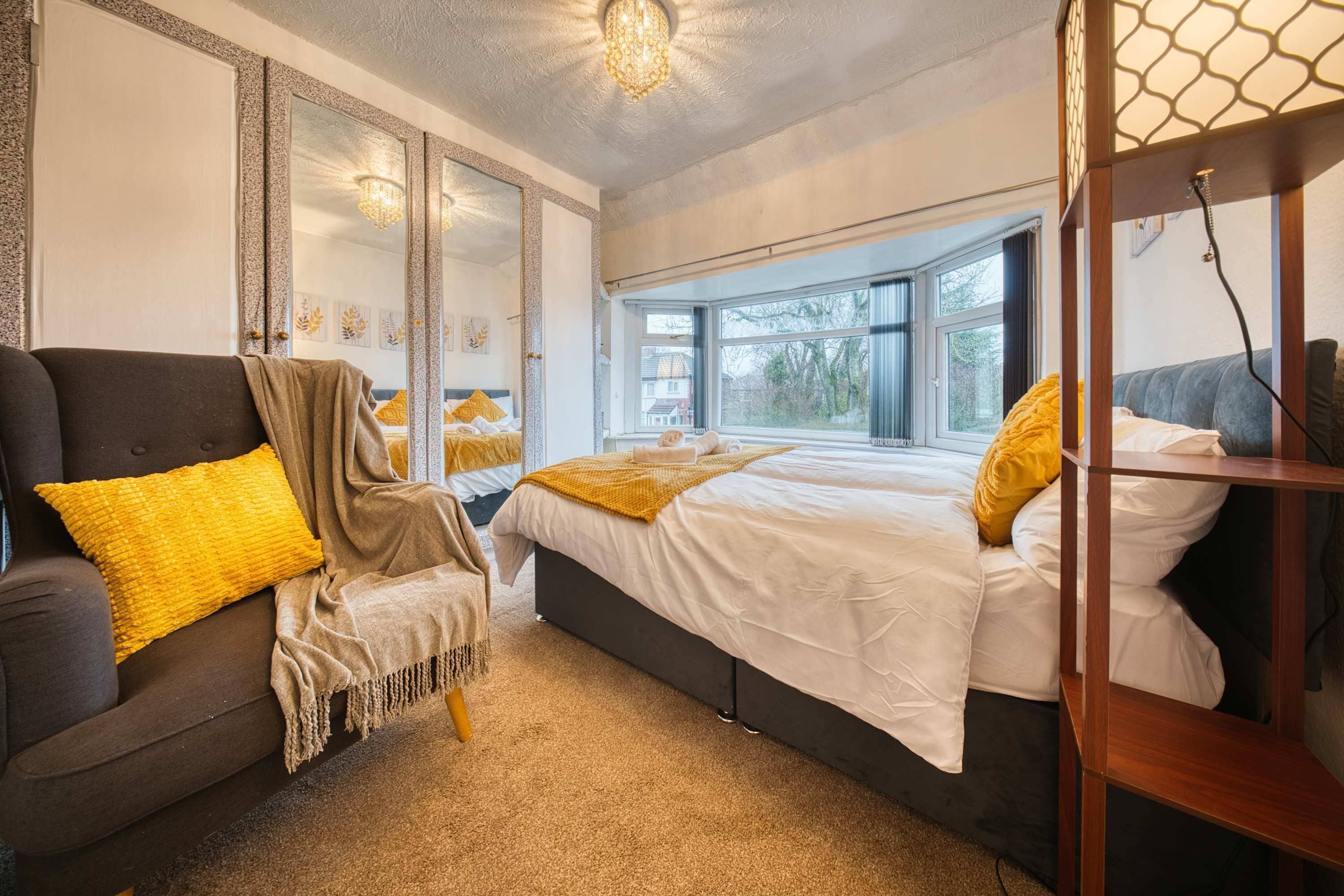 A bedroom with a bed, a chair, a window, and a mirror.