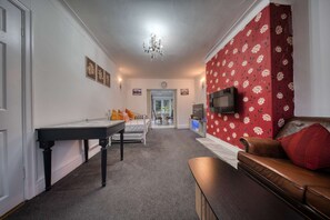 Una habitación de hotel con cama, escritorio, televisor y un papel tapiz rojo con motivos florales.