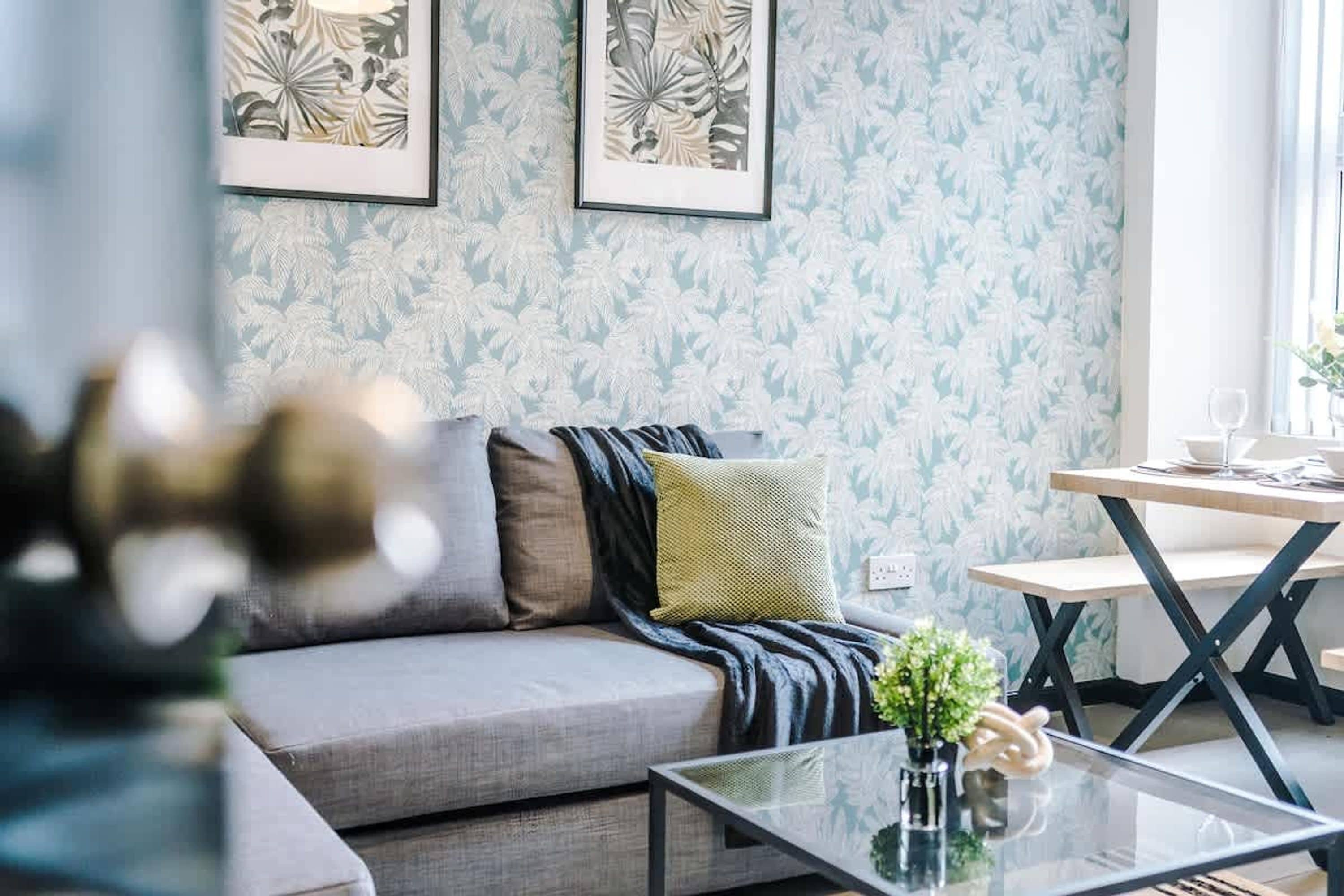 Ein Wohnzimmer mit einer Couch, einem Couchtisch und einem Esstisch mit Stühlen. An der Wand befinden sich zwei gerahmte Kunstwerke.