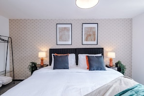 Une chambre d’hôtel avec un lit, deux tables de chevet avec des lampes, un mur orné d’un motif géométrique et deux tableaux encadrés au-dessus du lit.