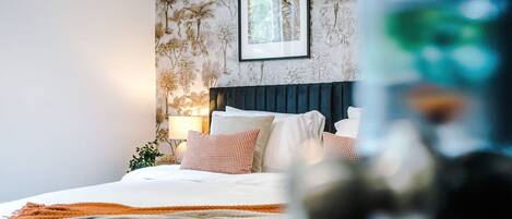 A neatly made bed with a white and orange blanket, a dark headboard, and a framed picture on the wall.