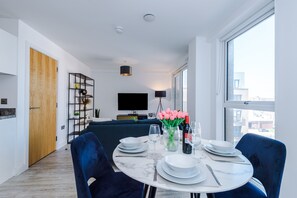 Una sala de estar moderna con comedor, estantería, televisor de pantalla plana y un amplio ventanal.