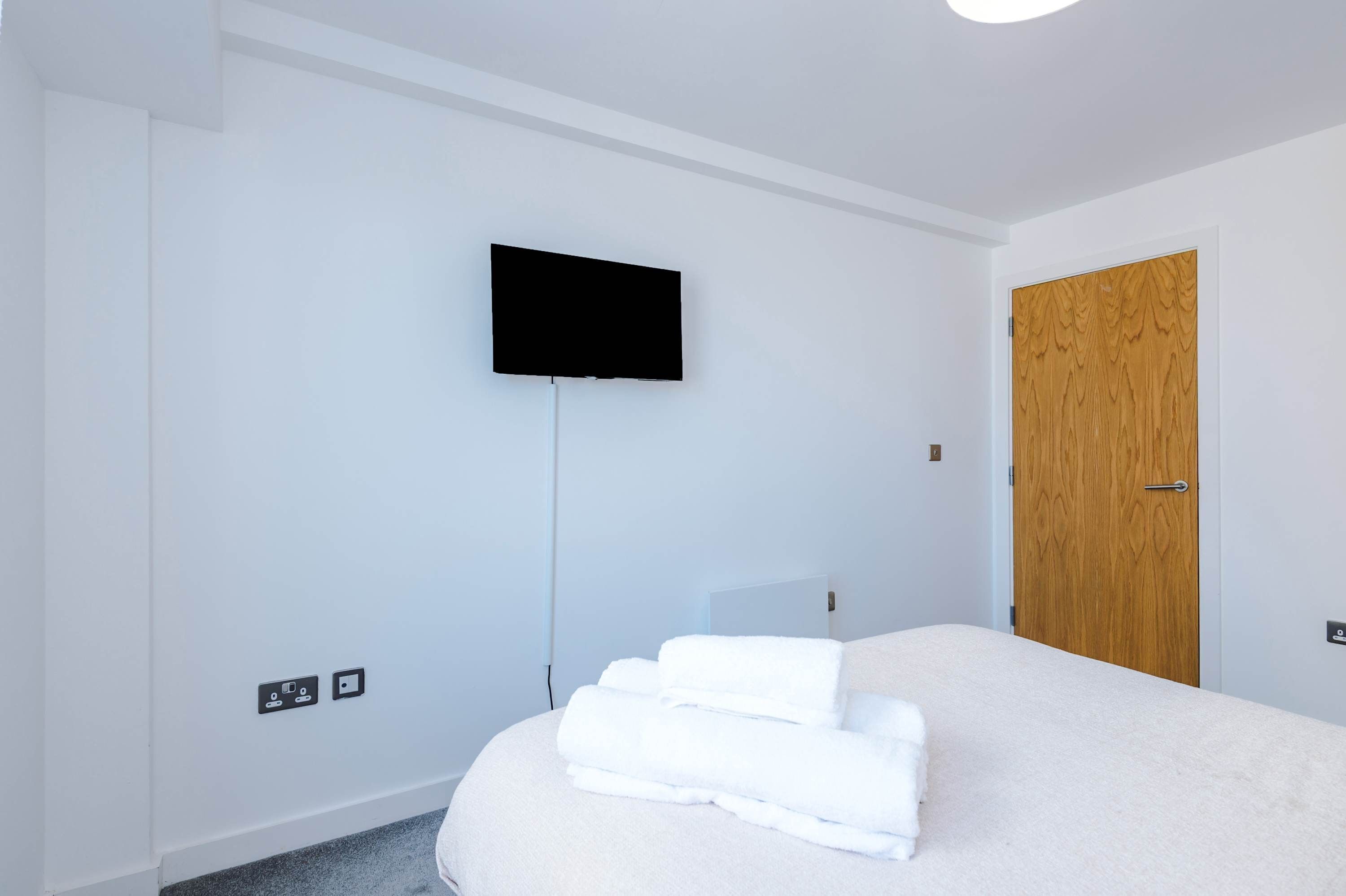 A hotel room with a bed, a television mounted on the wall, and a wooden door.