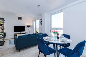 A modern living room with a sofa, a dining table set for two, and a television mounted on the wall. - Modern 2 Bed Duplex Free Parking Wi Fi (Salford)