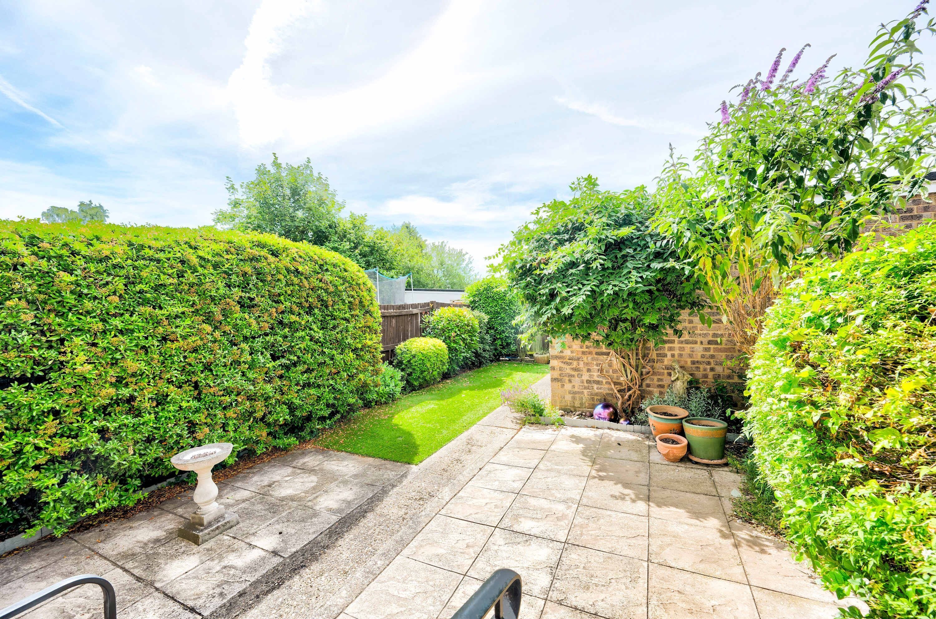 A well-maintained garden with a paved patio, a stone wall, and various plants.