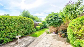 A well-maintained garden with a paved patio, a stone wall, and various plants.