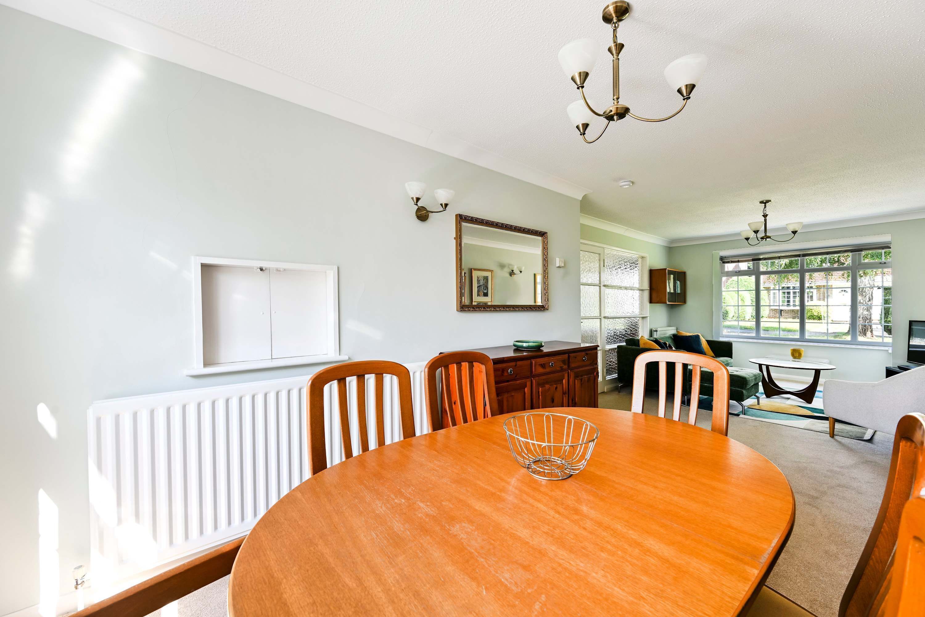A dining area with a wooden table, chairs, a radiator, a mirror, and a window with a view.