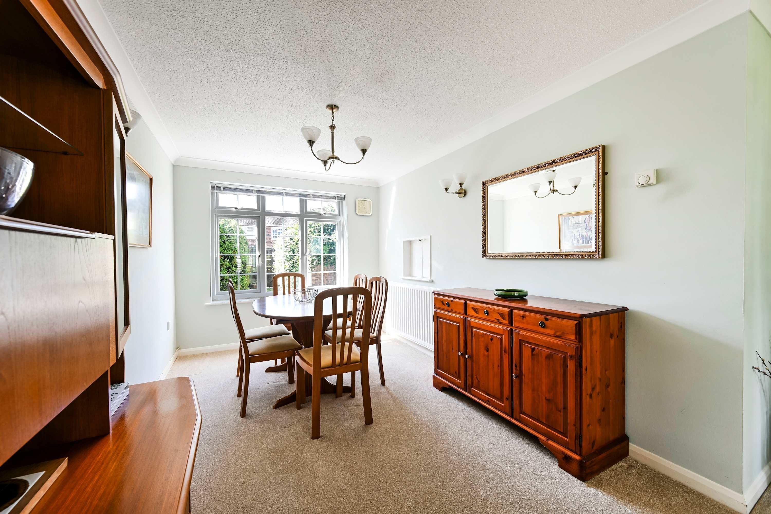 A dining area with a round table, chairs, a wooden cabinet, and a chandelier.