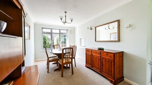 Een eetruimte met een ronde tafel, stoelen, een houten kast en een kroonluchter.