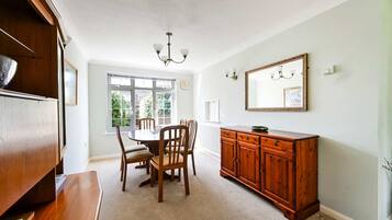 A dining area with a round table, chairs, a wooden cabinet, and a chandelier.
