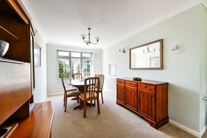 A dining area with a round table, chairs, a wooden cabinet, and a chandelier. - Spacious 3bed Home in Maidenhead Sleeps 6 (Maidenhead)