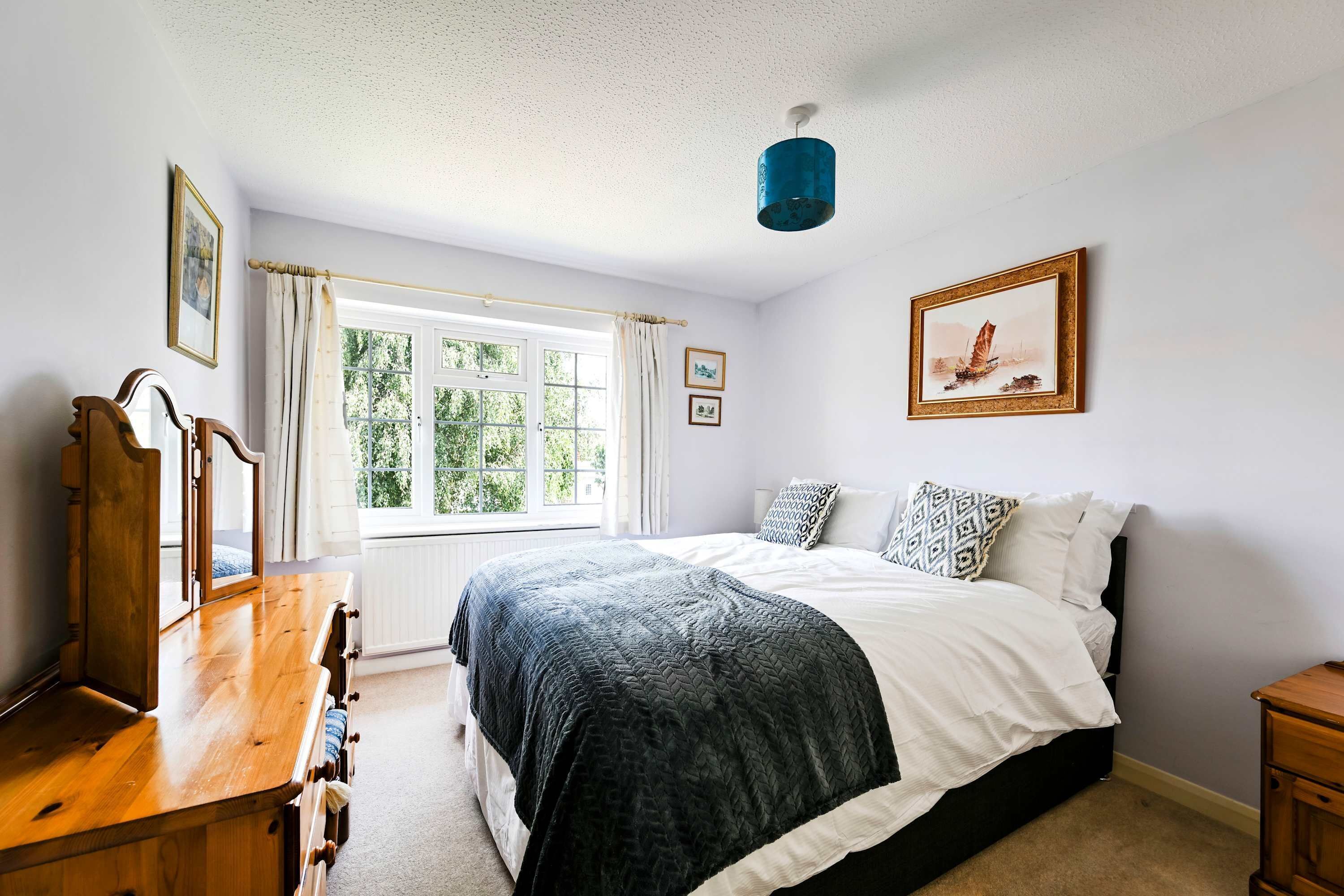 Une chambre à coucher avec un lit, une commode, une fenêtre avec des rideaux, un tableau au mur et un luminaire au plafond.