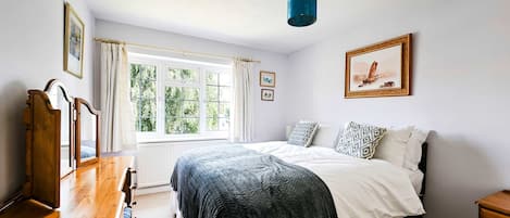 A bedroom with a bed, a dresser, a window with curtains, a painting on the wall, and a ceiling light.