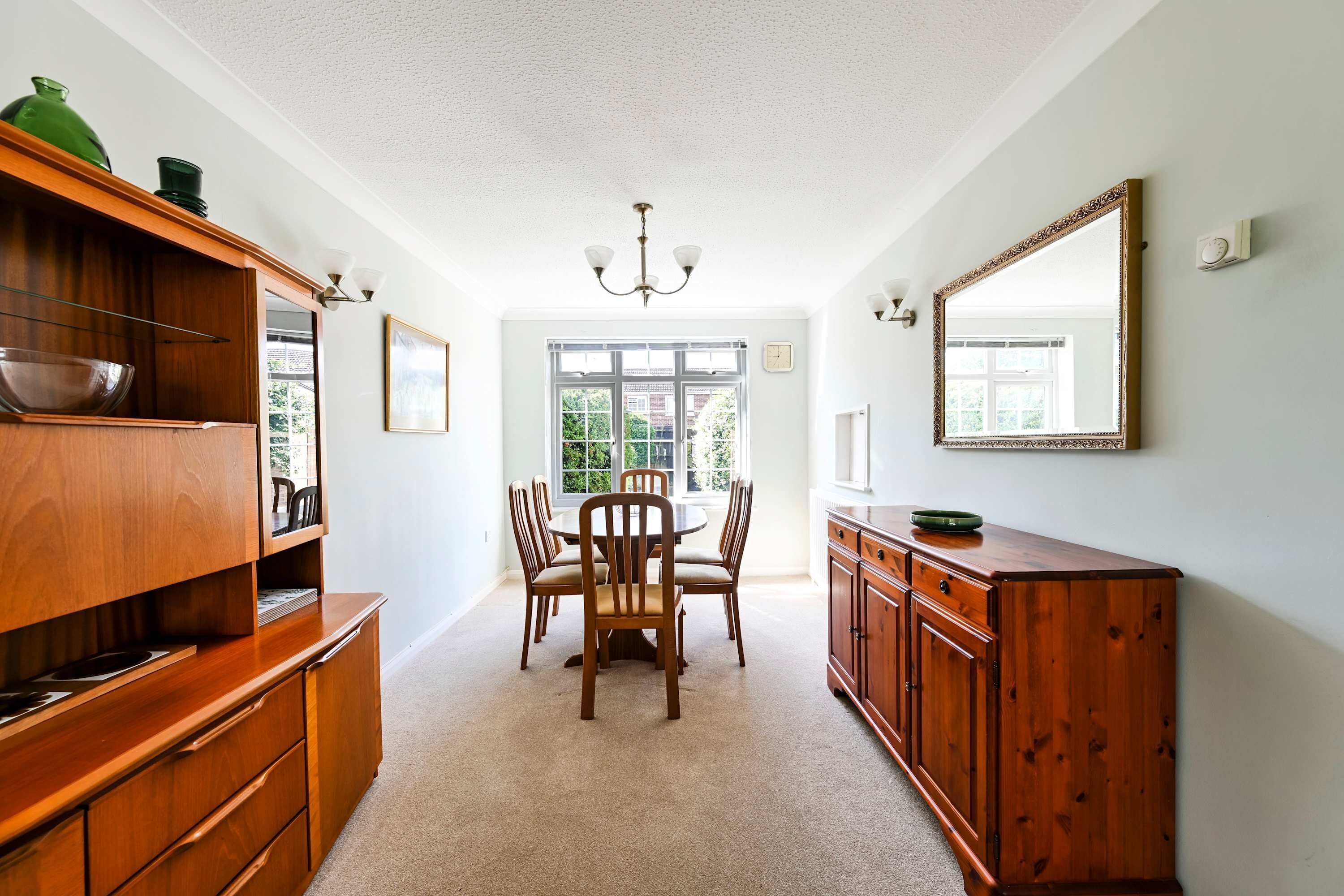 A dining area with a wooden table and chairs, a chandelier, and a large mirror on the wall.