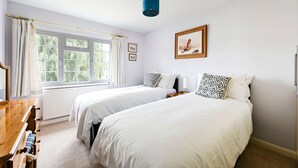Een slaapkamer met twee bedden, een raam met gordijnen, een houten dressoir en een lijst met een afbeelding aan de muur.