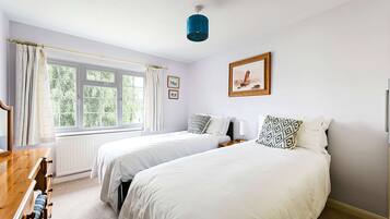 A bedroom with two beds, a window with curtains, a wooden dresser, and a framed picture on the wall.