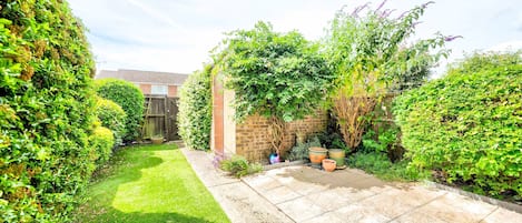 A well-maintained garden with a paved patio, a brick wall, and various plants.
