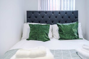 Ein Bett mit einer gesteppten Kopfteil, weißer Bettwäsche und zwei grünen Kissen.