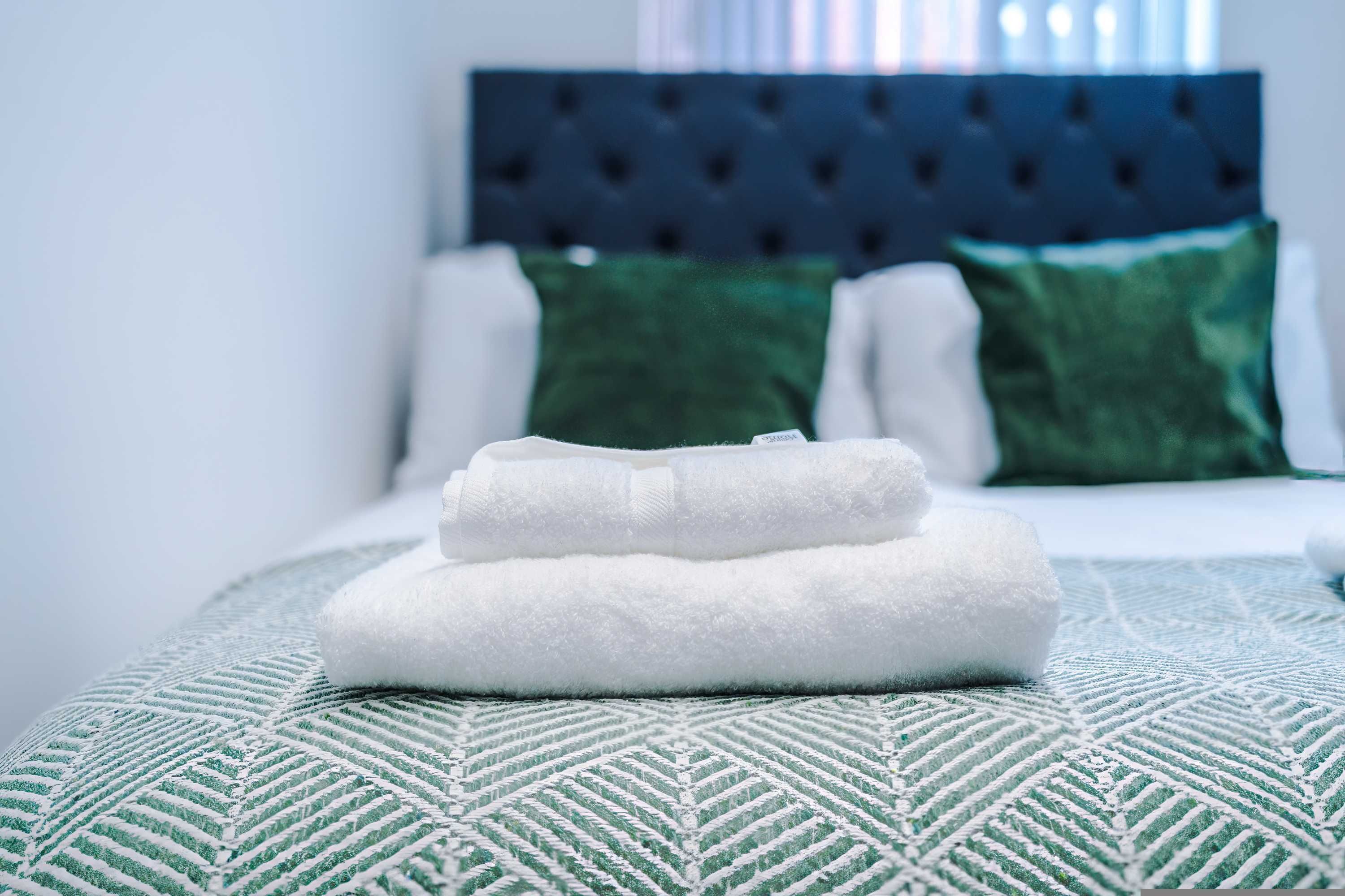 A neatly made bed with a patterned bedspread and two pillows, one green and one white, in a room with a dark headboard.