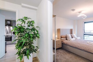 Ein modernes Schlafzimmer mit Bett, Nachttisch, Lampe und einer großen Topfpflanze.