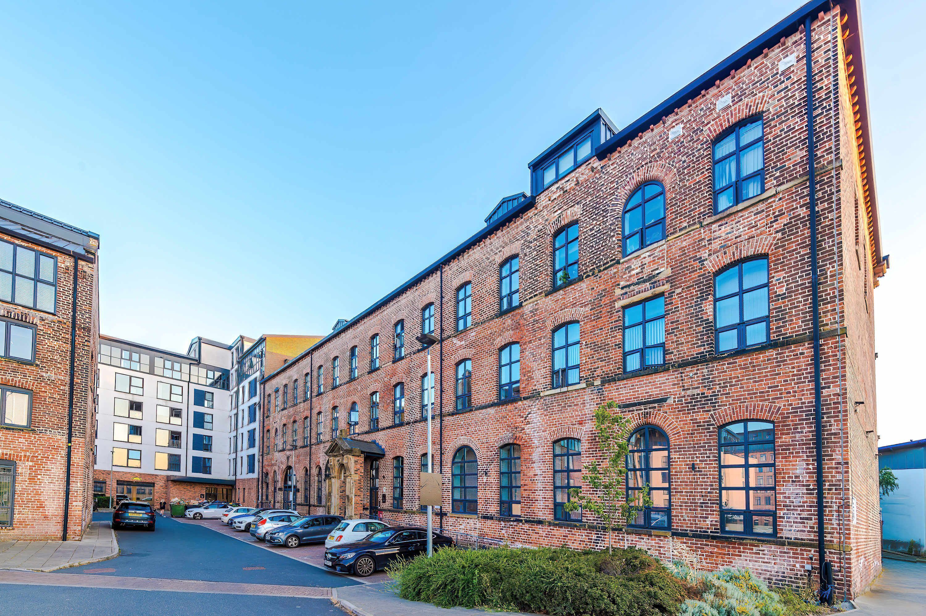 A multi-story brick building with large windows and a parking area in front.