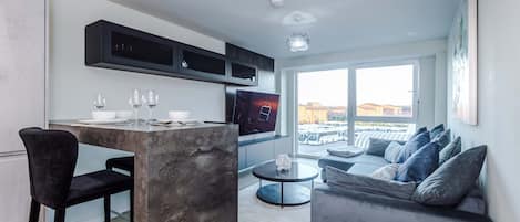 A modern living space with a kitchen area, a dining table with chairs, a sofa, and a television.