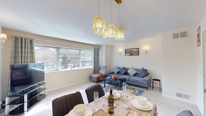Ein modernes Wohnzimmer mit einer Couch, Fernseher, Esstisch und einem großen Fenster.