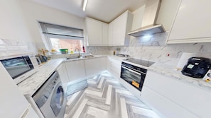 A modern kitchen with white cabinetry, a built-in oven, a microwave, and a coffee machine. - 2BR Reading Apt Near Station Near Hospital (Reading)