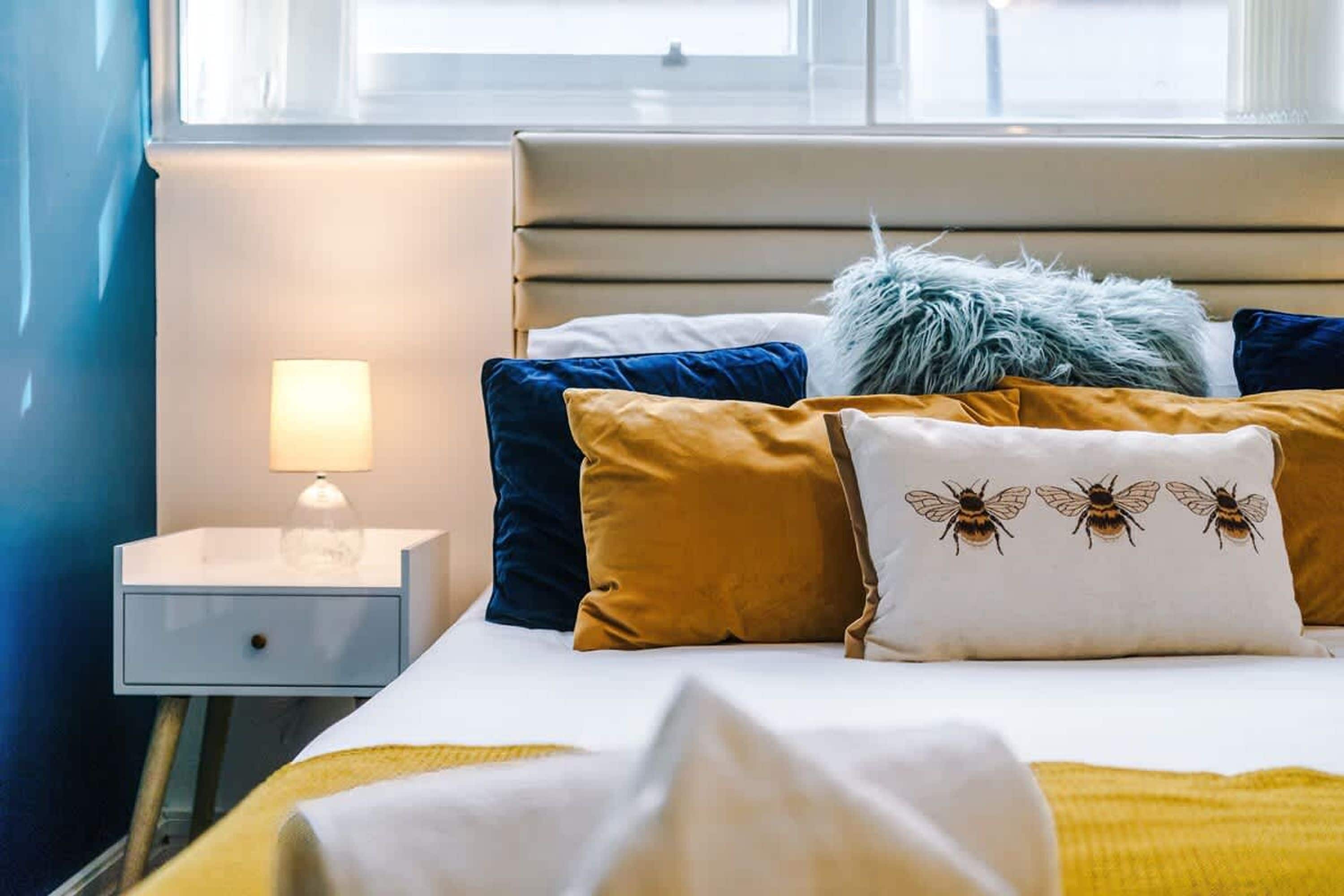 Ein ordentlich bezogenes Bett mit verschiedenen Kissen und einer Nachttischlampe.