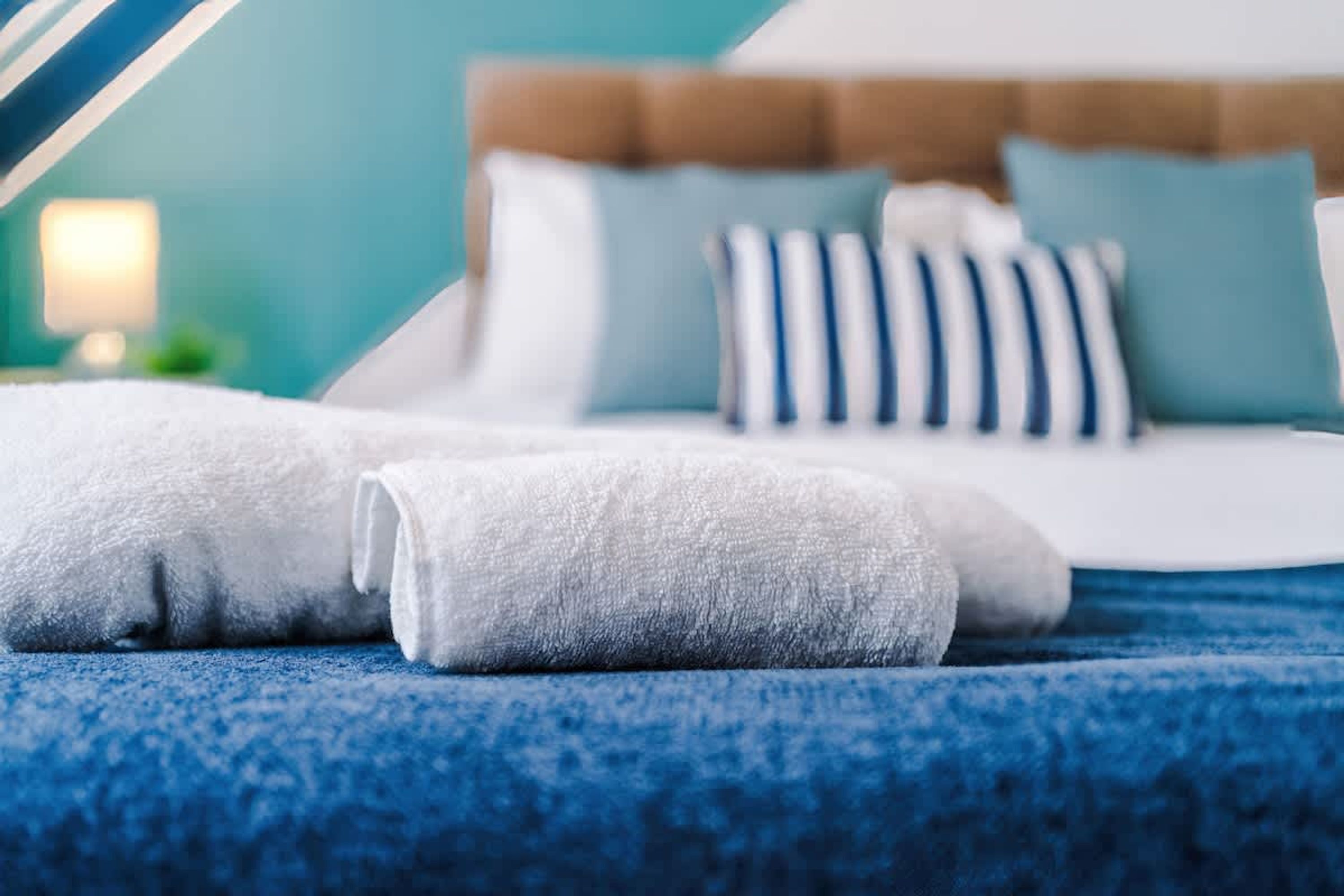 A neatly made bed with white linens and blue pillows, a blue textured bedspread, and a wooden headboard.