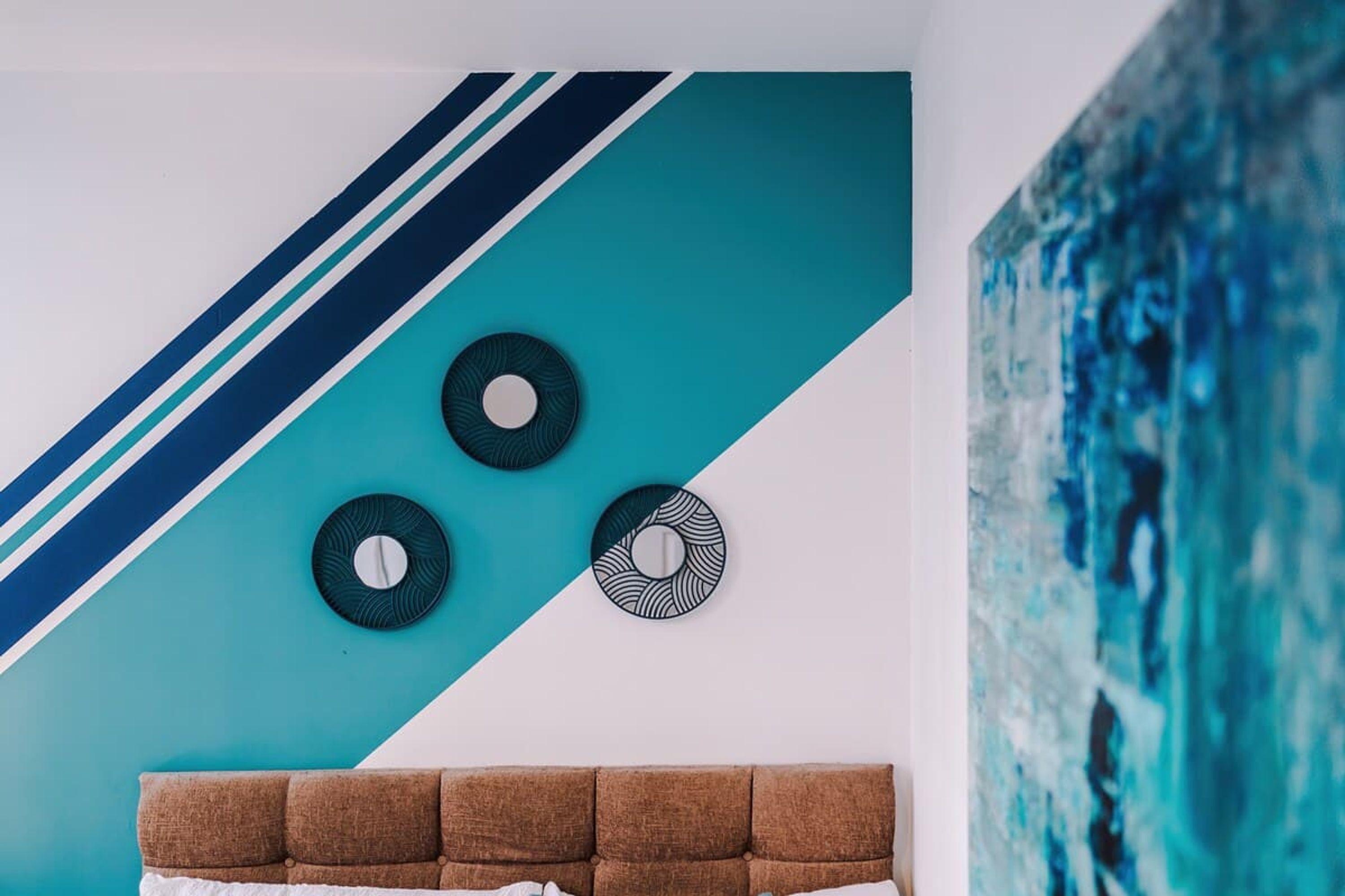 Een kamer met een wand in teal en wit, een bruin hoofdeinde en drie ronde decoraties aan de muur.