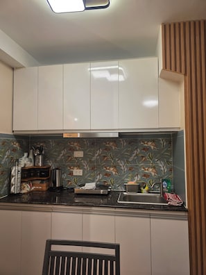 A kitchen with white cabinets, a black countertop, and a floral backsplash. - Condo near Mactan Beaches (Lapu-Lapu)