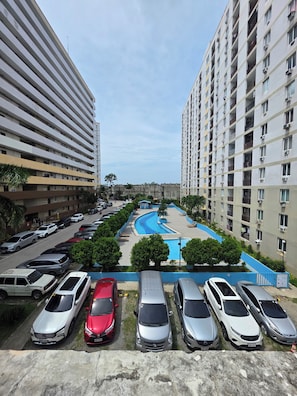 A residential building with multiple floors, a swimming pool, and a parking lot with several cars. - Condo near Mactan Beaches (Lapu-Lapu)
