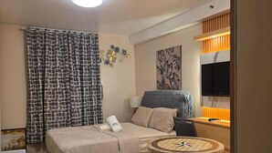 Ett hotellrum med en säng, ett runt bord, en stol, en tv och en väggklocka.