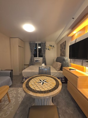 A hotel room with a bed, a desk, a television, a round table, and a window with curtains. - Condo near Mactan Beaches (Lapu-Lapu)