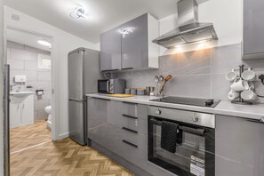 A modern kitchen with grey cabinetry, a built-in oven, microwave, and a stainless steel range hood. - Sleek 2BR Whitefield Parking 5m to Metrolink (Manchester)