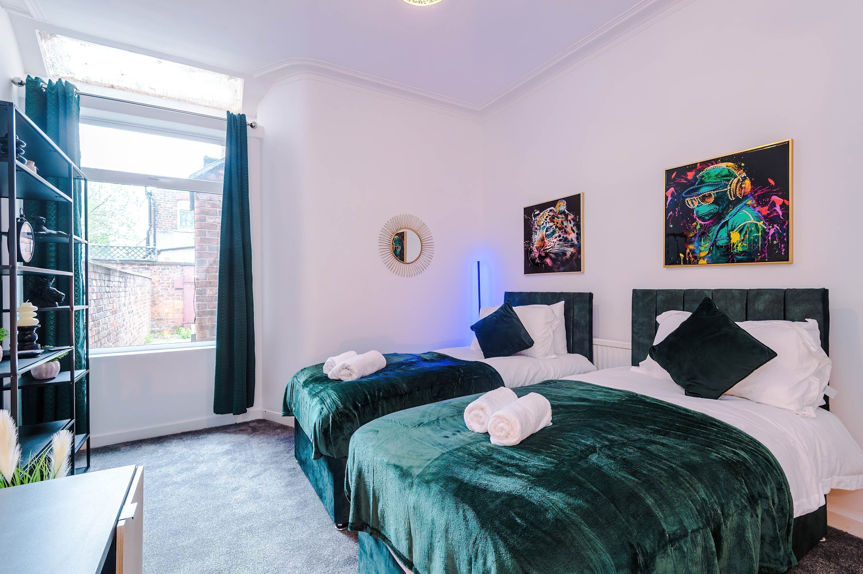 A hotel room with two beds, a large window, a bookshelf, and artwork on the walls.