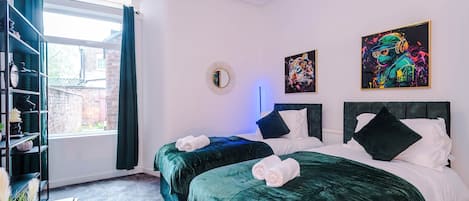 A hotel room with two beds, a large window, a bookshelf, and artwork on the walls.