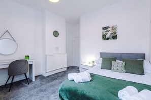 Ein Hotelzimmer mit einem Bett, einem Schreibtisch, einem Stuhl, einem Heizkörper, einer Wanduhr und einem Wandbild.